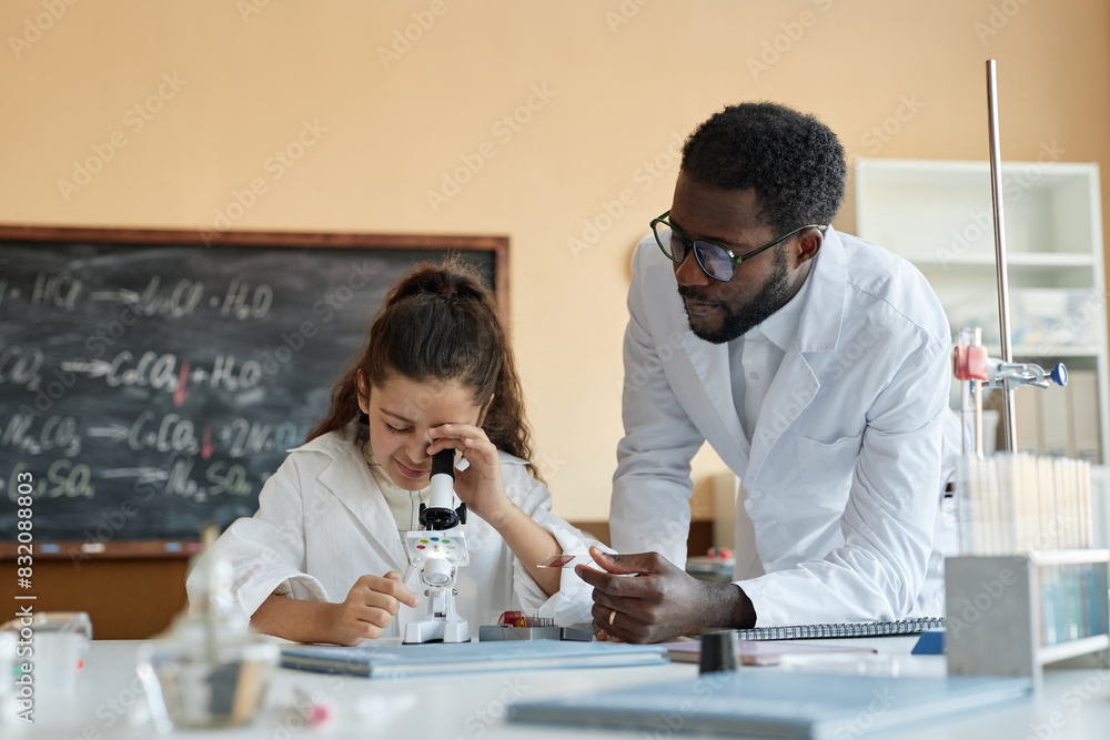 Young African American teacher of Chemistry wearing lab coat giving microscope slide to Middle Eastern student, copy space Young African American teacher of Chemistry wearing lab coat giving microscope slide to Middle Eastern student, copy space