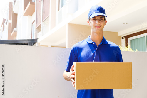Delivery man in blue uniform. A male employee in a cap t-shirt working as courier dealer hold empty cardboard box. Young courier holding parcels on doorstep. Delivery service concept © artitwpd