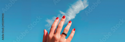A woman s hand adorned with red painted nails and a black ring on the pinky finger reaches out into the vast expanse of a blue sky creating a beautiful copy space image 200 characters photo