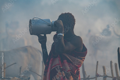 Backlight photo of a man in a Mundari cattle camp drinking milk, Mundari tribe, South Sudan photo