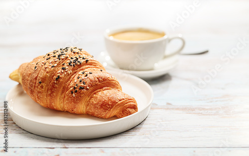 Freshly baked Croissant and a cup of Coffee artfully presented on a White Wooden Table