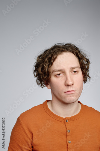 Vertical medium closeup studio portrait of young Caucasian posing for camera with uninterested facial expression, copy space photo