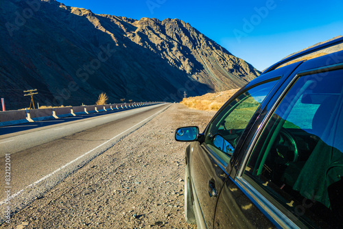 Black motor vehicle on the side of the asphalt road, with majestic mountains in the background.