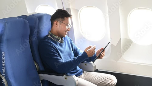Young Asian executive excels in first class, multitasking with digital tablet, laptop and smartphone. Travel in style, work