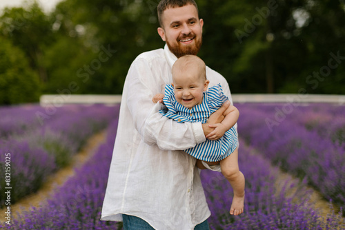 A bearded man in a white shirt is lifting baby in air on a lavender field. Daddy is lifting up daughter and have fun. 