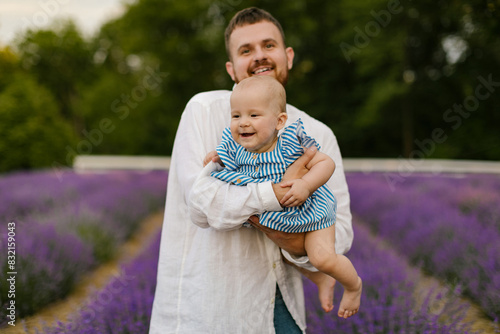 A bearded man in a white shirt is lifting baby in air on a lavender field. Daddy is lifting up daughter and have fun. 