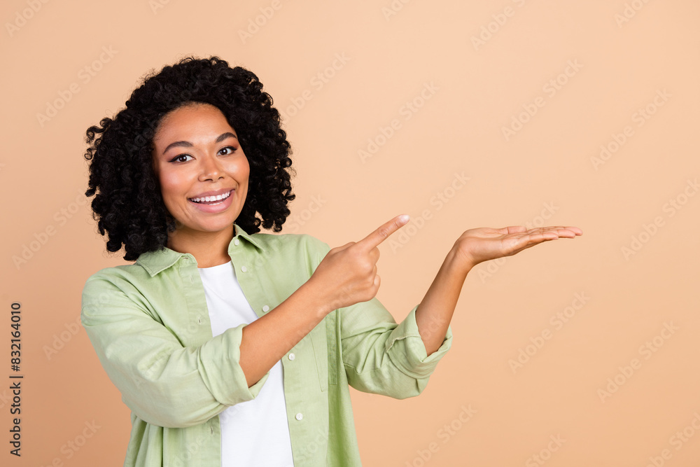 Photo of nice young lady point finger hold empty space wear green shirt isolated on beige color background Photo of nice young lady point finger hold empty space wear green shirt isolated on beige color background