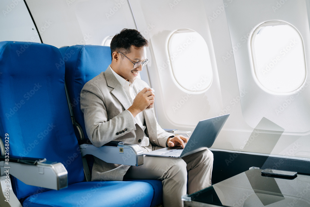 Attractive Asian male passenger of airplane sitting in comfortable seat while working laptop and tablet with mock up area using wireless connection. Attractive Asian male passenger of airplane sitting in comfortable seat while working laptop and tablet with mock up area using wireless connection.