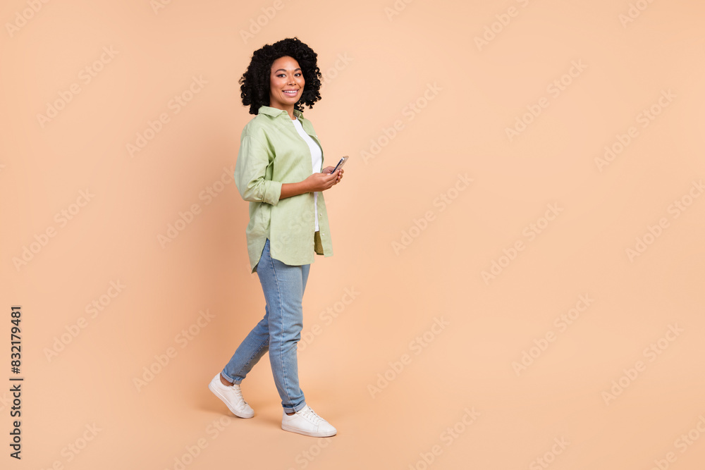 Full size photo of nice young lady smart phone walk empty space wear shirt isolated on beige color background Full size photo of nice young lady smart phone walk empty space wear shirt isolated on beige color background