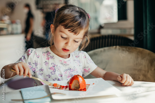 A cute little girl 4-5 years old enjoying a slice of cake in a restaurant