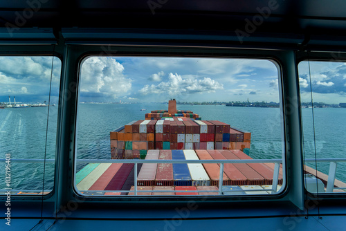 A view from a ship's bridge window overlooking a large stack of colorful shipping containers on the vessel's deck, with the ocean and cloudy sky in the background. photo