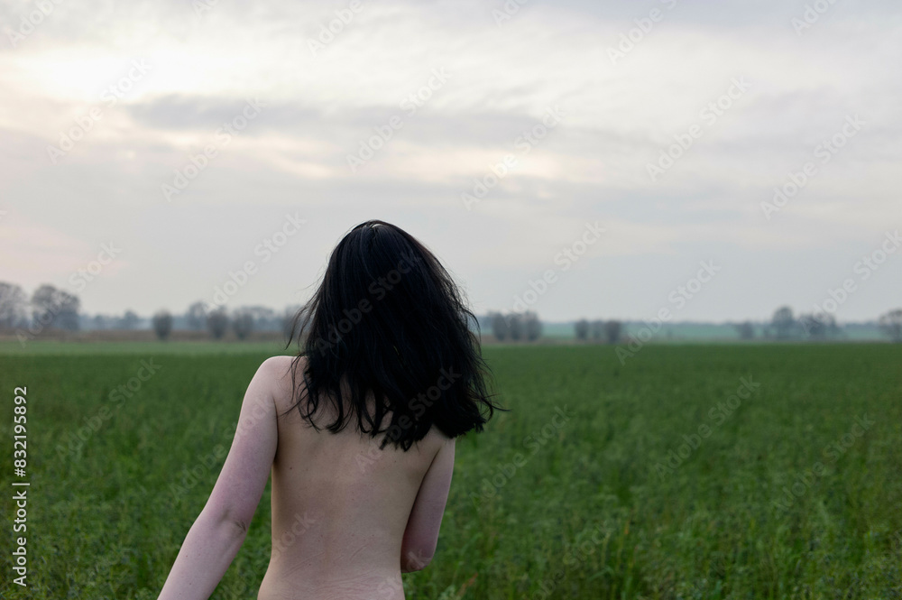 A person with black hair stands in a green field looking towards a cloudy sky at dusk. A person with black hair stands in a green field looking towards a cloudy sky at dusk.