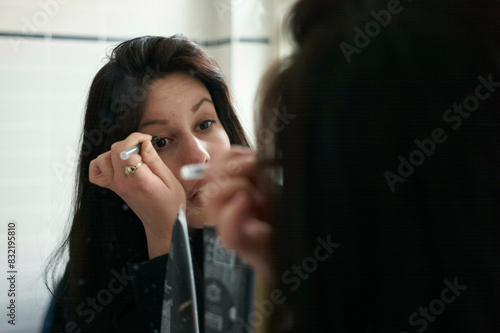 A woman is applying mascara to her eyelashes while looking into a mirror. photo