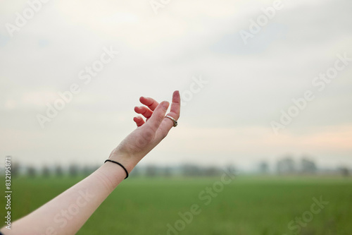 An outstretched arm reaching towards the sky with an open hand against a background of a blurred green field and a pale sky. photo