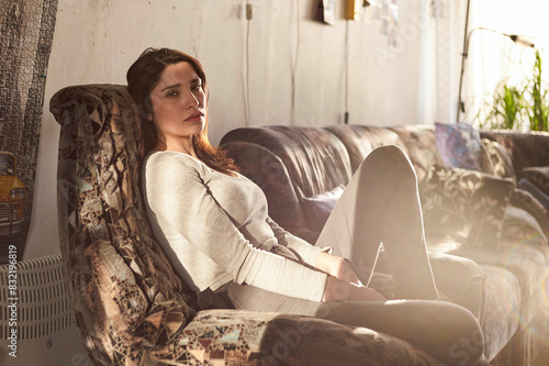 A woman is seated on a patterned sofa in a warmly lit room, gazing thoughtfully to the side. photo