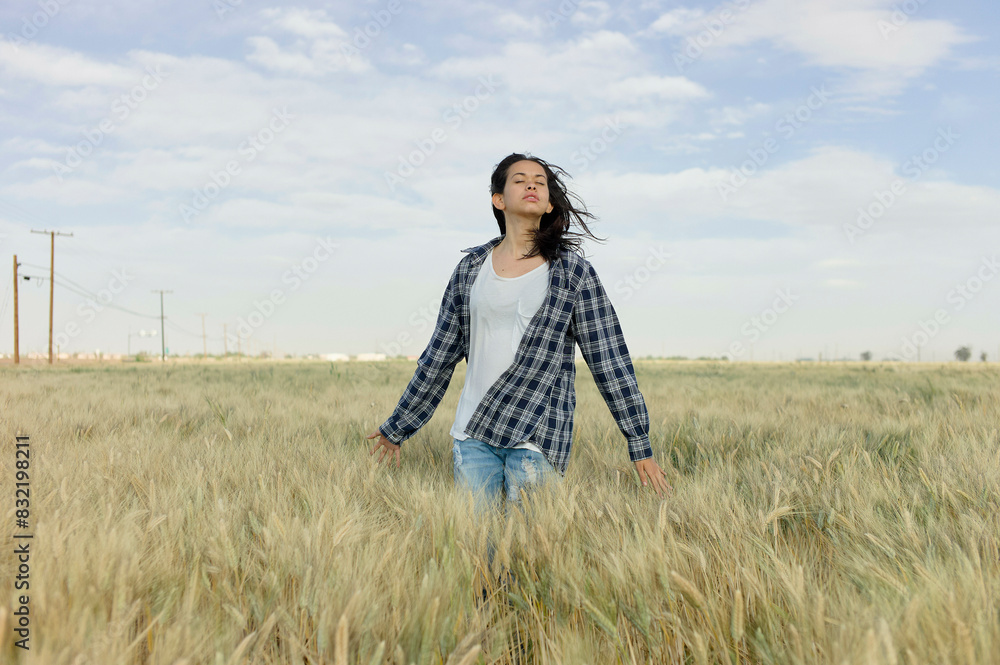 A woman stands in a wheat field with her arms outstretched and eyes closed, embracing the open space. A woman stands in a wheat field with her arms outstretched and eyes closed, embracing the open space.