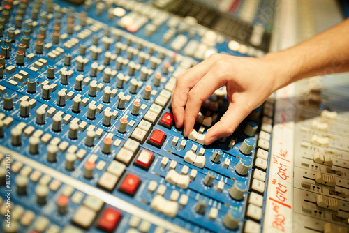 A hand adjusting a knob on a professional audio mixing console with numerous buttons and sliders.  photo