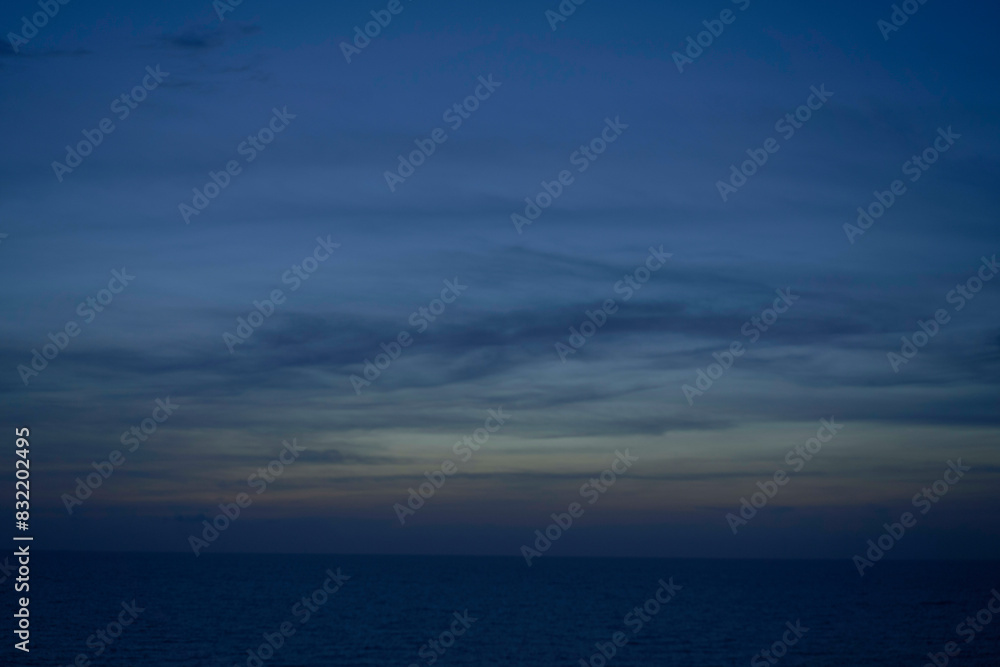 A calm ocean horizon under a twilight sky with subtle gradients from deep blue to orange near the horizon, and streaks of clouds above. A calm ocean horizon under a twilight sky with subtle gradients from deep blue to orange near the horizon, and streaks of clouds above.
