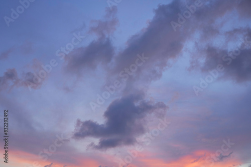 The image displays a serene twilight sky with soft pink and purple hues accented by dark, wispy clouds. photo