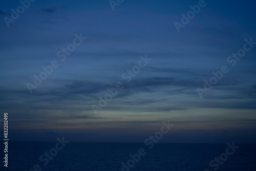 A calm ocean horizon under a twilight sky with subtle gradients from deep blue to orange near the horizon, and streaks of clouds above. photo
