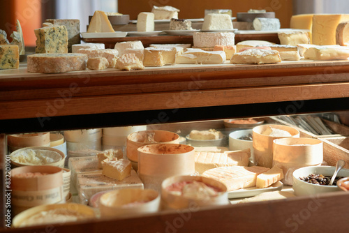 A variety of cheeses are elegantly displayed in a wooden case, illuminated by warm light, showcasing an assortment of textures and colors.