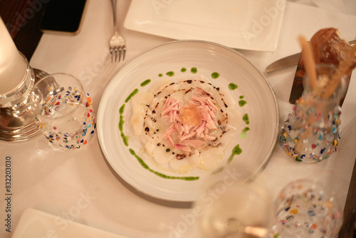 This is an over-the-top view of a finely plated dish, possibly a salad, surrounded by elegant glassware on a white tablecloth.
