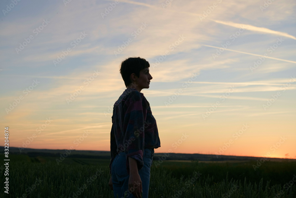 A profile view of a person standing in a field at sunset, with the horizon line and colorful sky in the background. A profile view of a person standing in a field at sunset, with the horizon line and colorful sky in the background.