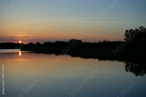 A serene sunset scene over a calm lake with reflections of the diminishing sun and silhouetted landscape against a gradient evening sky. photo