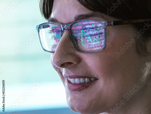 A close-up of a smiling woman wearing glasses that are reflecting a colorful graph. The image focuses on her profile, showcasing her glasses and joyful expression.