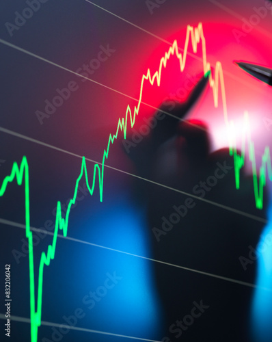 A blurred silhouette of a person is seen in the foreground with a background of a stock market chart displaying a fluctuating trend line in red and green.