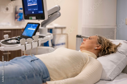 A woman lies on a medical examination table next to an ultrasound machine, appearing calm and awaiting a procedure. photo