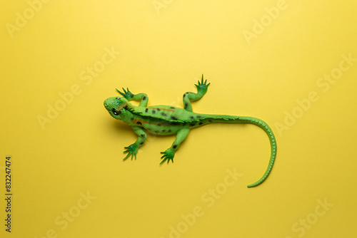 Green lizard toy on bright yellow background. Minimal art concept.