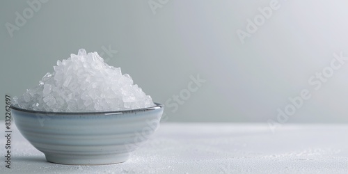 Bowl of white crystals on pale surface, minimalist design © Larisa