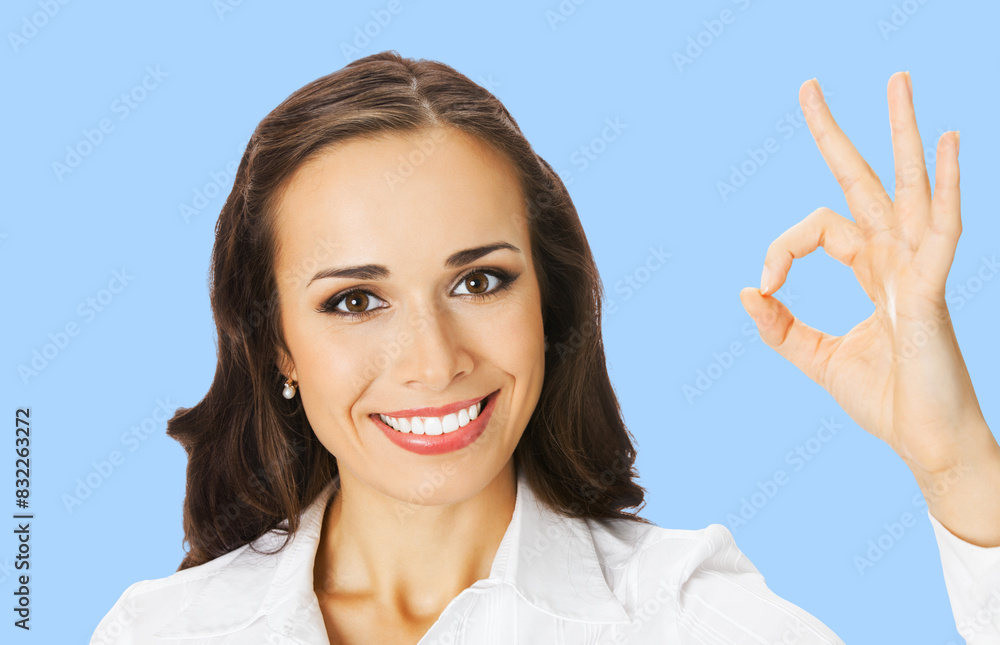 Businesswoman in white confident clothing showing ok okay hand sign, isolated pastel plain blue background. Portrait of happy smiling gesturing brunette woman at studio. Business concept photo. Businesswoman in white confident clothing showing ok okay hand sign, isolated pastel plain blue background. Portrait of happy smiling gesturing brunette woman at studio. Business concept photo.