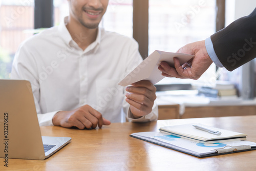 Good job Asian manager business man giving financial reward in an envelope, business letter extra salary to company employee, male worker office hand received premium bonus, getting cheque from boss. photo