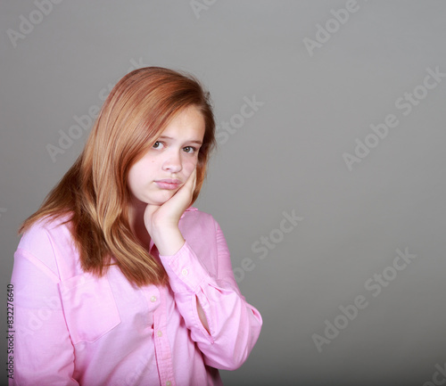 A girl with long red hair is wearing a pink shirt and is looking down