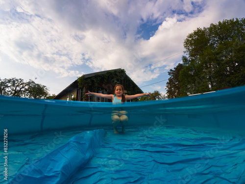 A little girl child splashes in an improperly installed inflatable pool on the street near the house in the summer. photo