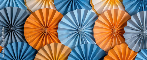 Abstract paper fans in various shades of orange  blue and grey are arranged to create an intricate pattern. The fans are arranged in the style of pointillism to form an abstract design.