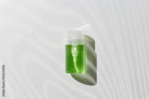 Pump dispenser with green liquid for skin treatment, beauty routine, skin health. Cosmetic product lotion, serum, micellar water mockup with sun shadow on white background, minimal flat lay