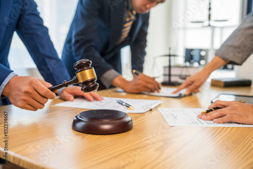 A team meeting of business people and a lawyer in formal suits is taking place at a desk, discussing a contract and various aspects of the law and litigation.