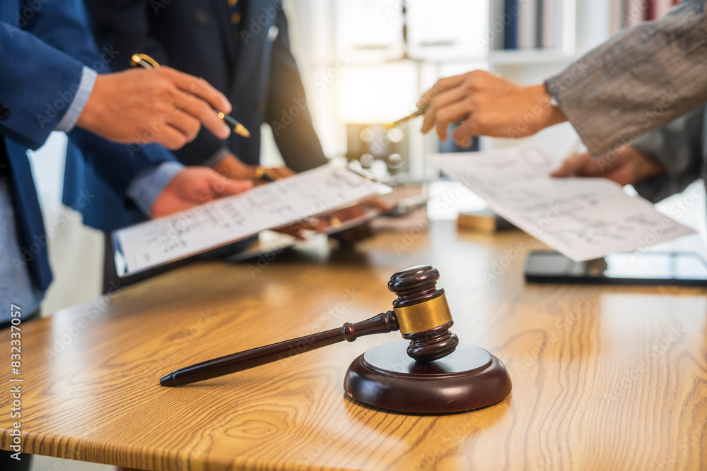 A team meeting of business people and a lawyer in formal suits is taking place at a desk, discussing a contract and various aspects of the law and litigation. A team meeting of business people and a lawyer in formal suits is taking place at a desk, discussing a contract and various aspects of the law and litigation.