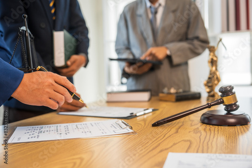 A team meeting of business people and a lawyer in formal suits is taking place at a desk, discussing a contract and various aspects of the law and litigation.