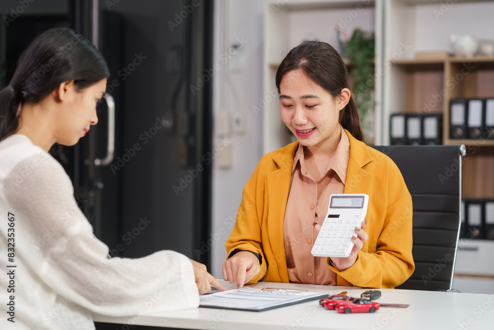 Fototapeta premium Asian businesswoman and a salesman discuss car sales, insurance, and financing with a customer at a desk, covering used car loans, premiums, deductibles, and various insurance coverage options.