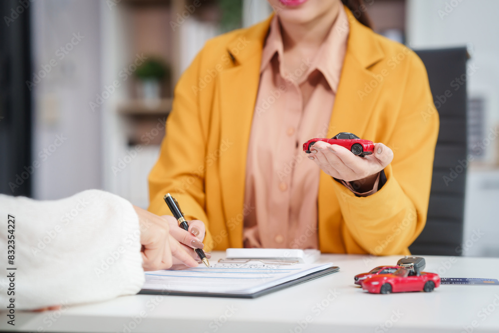 Fototapeta premium Asian businesswoman and a salesman discuss car sales, insurance, and financing with a customer at a desk, covering used car loans, premiums, deductibles, and various insurance coverage options.