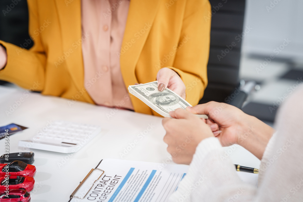 © NanSan - Asian businesswoman hands car keys to a customer while a salesman discusses car sales, insurance, used car loans, and finance options at a desk, covering premiums and coverage types.