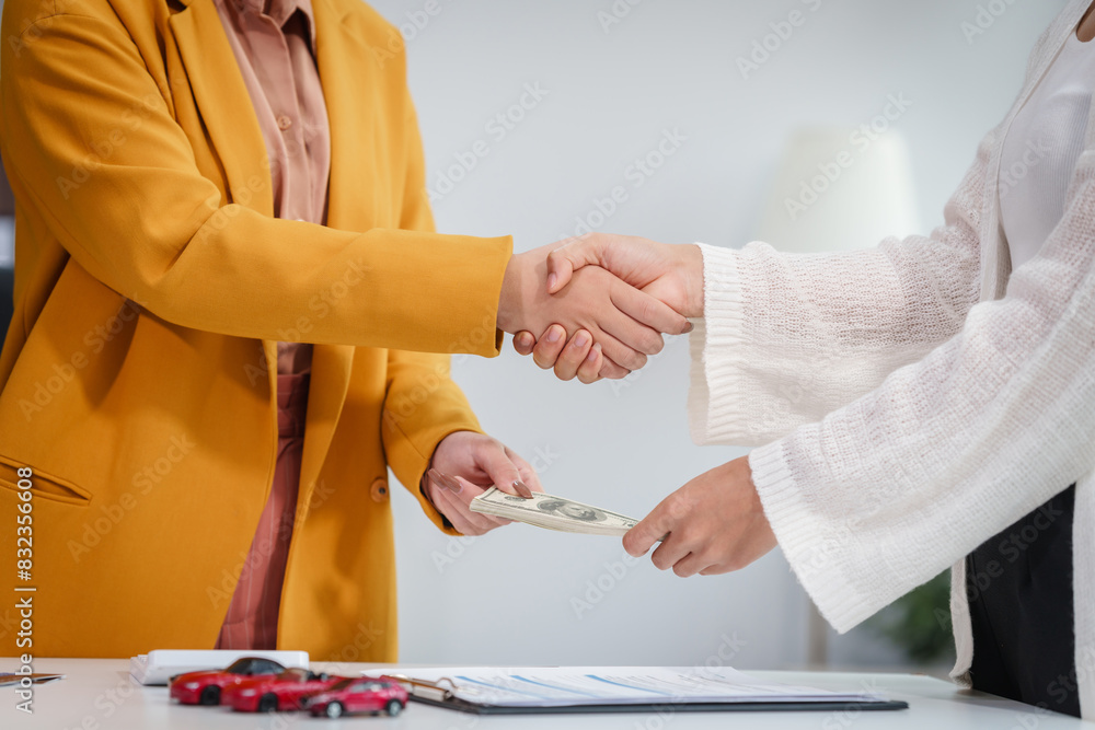 Obraz premium Asian businesswoman hands car keys to a customer while a salesman discusses car sales, insurance, used car loans, and finance options at a desk, covering premiums and coverage types.