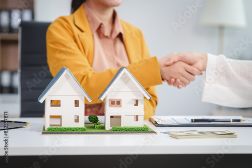 Asian businesswoman discusses home purchase contracts with clients at her desk, focusing on loans, mortgages, and other financial aspects of real estate transactions.
