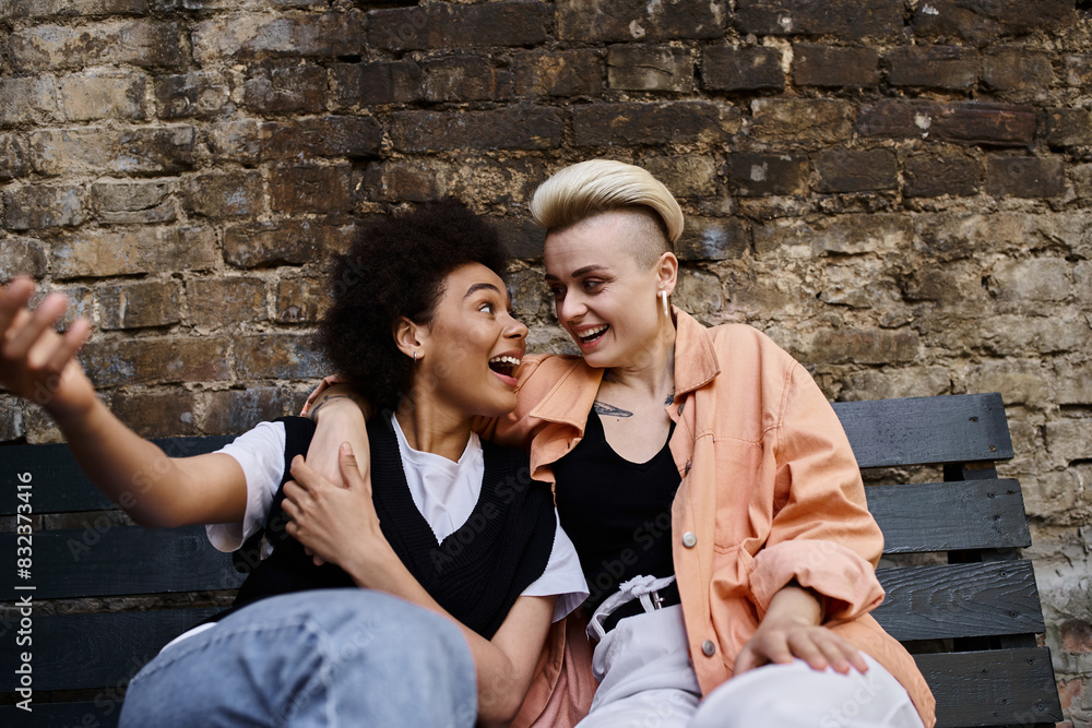 Two diverse women sit on top of a wooden bench, enjoying a peaceful moment together. Two diverse women sit on top of a wooden bench, enjoying a peaceful moment together.