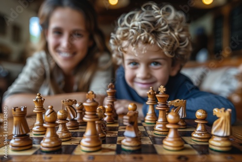 Two children are playing chess together, with the focus on a young boy who is smiling at the camera