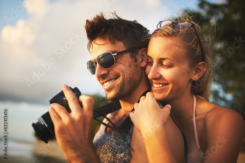Man, woman and camera at beach for sunset, travel and vacation to island in summer for love. Happy, couple and photography for social media, holiday and blog with smile and sunshine for date in Bali photo